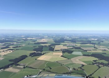Aéronef survolant un paysage rural près d'un aérodrome.