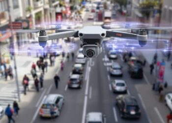 Drone survolant une rue avec voitures et piétons visibles.