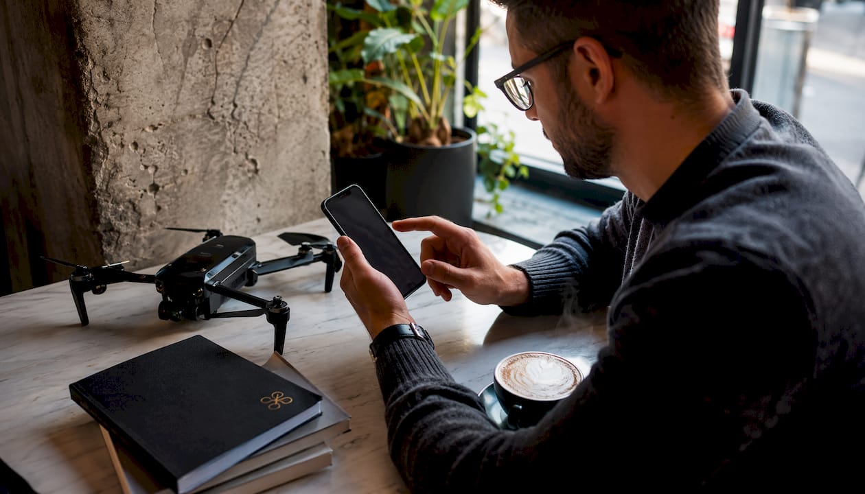 Une personne utilise une application de réglementation des drones sur son smartphone, confortablement installée à l'intérieur.