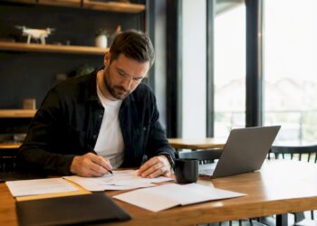 Des mains trient et classent des dossiers de contrats liés aux drones sur un bureau.