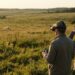 Télépilote en lunettes FPV et observatrice côte à côte dans une prairie, suivant un petit drone fait maison au soleil couchant
