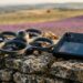 Drone 360° caréné posé sur un muret de pierres sèches à côté d’une radiocommande à écran, champ de lavande flou au coucher du soleil