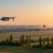 Drone en vol stationnaire au coucher du soleil, avec une base aérienne floue au loin