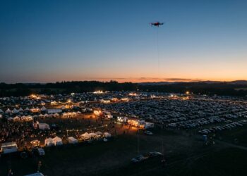 Drone relié au sol par un câble, en surveillance au-dessus d’un grand site événementiel au crépuscule