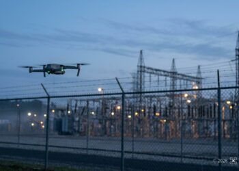 Petit drone en vol près de la clôture d’un site industriel sensible à la tombée de la nuit