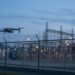 Petit drone en vol près de la clôture d’un site industriel sensible à la tombée de la nuit