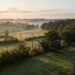Ligne électrique moyenne tension traversant un bocage au lever du soleil, avec un petit drone qui longe les câbles