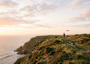 Randonneur sur un sentier de falaise au lever du soleil, suivi par un petit drone