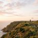 Randonneur sur un sentier de falaise au lever du soleil, suivi par un petit drone