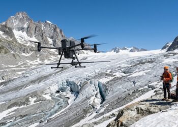 Drone équipé d’une antenne radar survolant un glacier alpin crevassé, deux alpinistes en veste orange au bord de la glace (illustration)