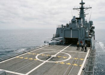 Drone hélicoptère à décollage vertical sur la plateforme arrière d’une frégate en mer, trois marins à distance
