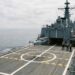 Drone hélicoptère à décollage vertical sur la plateforme arrière d’une frégate en mer, trois marins à distance