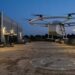 Drone de livraison décollant d’une aire derrière un entrepôt à la tombée de la nuit, maisons au fond