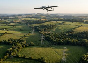 Drone à voilure fixe en vol au-dessus d’une ligne à haute tension traversant bocage et forêts