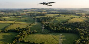 Drone à voilure fixe en vol au-dessus d’une ligne à haute tension traversant bocage et forêts