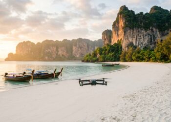 Drone en vol au-dessus d’une plage de Thaïlande bordée de falaises calcaires et de bateaux longtail