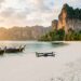 Drone en vol au-dessus d’une plage de Thaïlande bordée de falaises calcaires et de bateaux longtail
