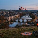 Télépilote au crépuscule observant un hélicoptère au-dessus d'une ville, illustration du salon European Rotors à Lyon