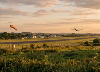 Aérodrome au coucher du soleil, manche à air au premier plan et avion au décollage