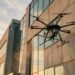 Drone de nettoyage hexacoptère pulvérisant un revêtement sur la façade en béton d’un immeuble de bureaux au coucher du soleil