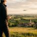 Télépilote de dos pilotant un drone au-dessus d’un village français au coucher du soleil