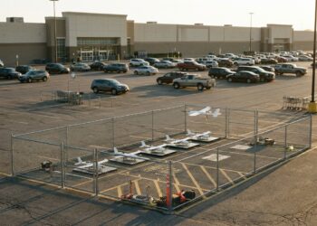 Drones de livraison sur leurs aires dans un enclos grillagé, sur le parking d’un hypermarché au soleil couchant