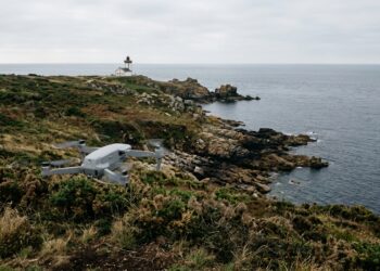 Drone en vol stationnaire au-dessus d’une côte rocheuse avec un phare